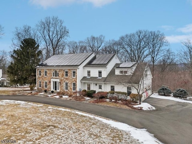 view of front of property featuring driveway, stone siding, and roof mounted solar panels