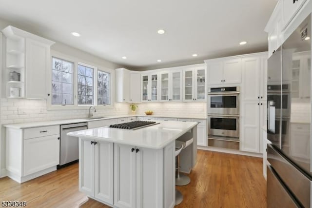 kitchen featuring stainless steel appliances, a sink, white cabinets, light countertops, and a center island