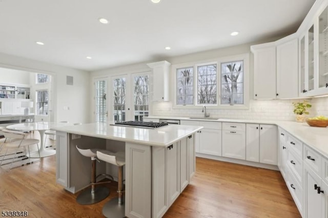 kitchen with a center island, gas stovetop, white cabinets, a sink, and light wood-type flooring