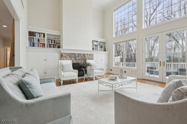 living room featuring french doors, wood finished floors, a high ceiling, crown molding, and a stone fireplace