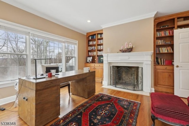 office area with built in shelves, light wood finished floors, a fireplace with flush hearth, ornamental molding, and baseboards