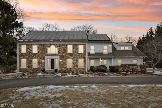 view of front of property featuring a standing seam roof, stone siding, metal roof, and solar panels