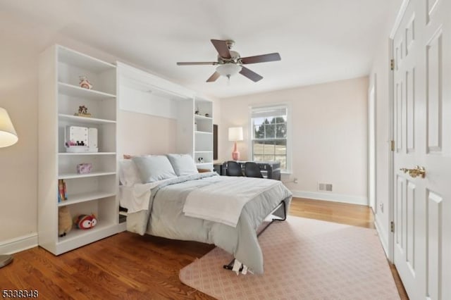 bedroom featuring a ceiling fan, baseboards, visible vents, and wood finished floors