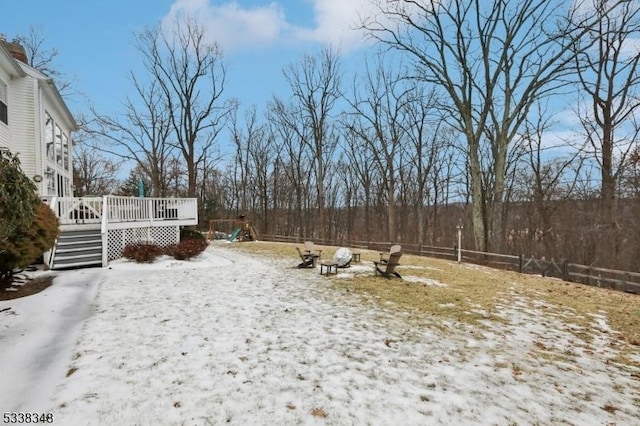 yard covered in snow with fence, a playground, and a wooden deck