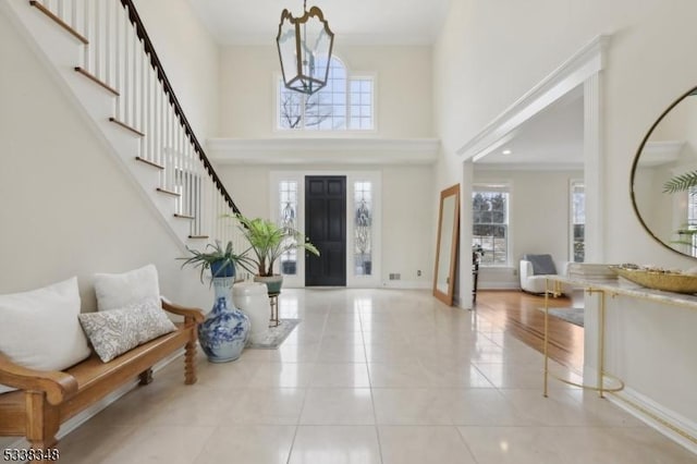 tiled foyer featuring crown molding, a notable chandelier, stairway, a towering ceiling, and baseboards