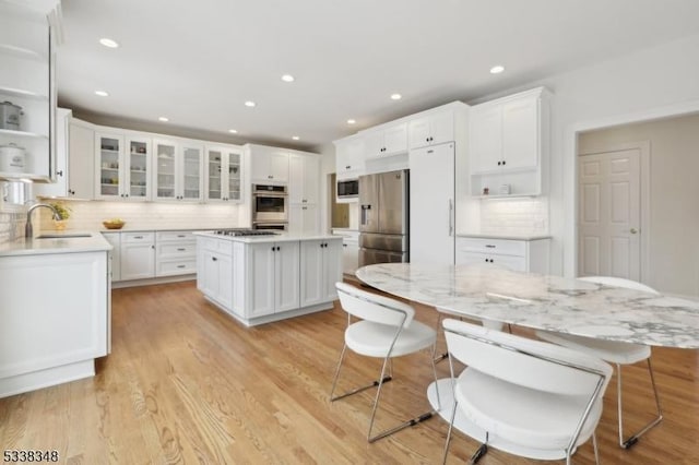 kitchen featuring a kitchen island, stainless steel appliances, light wood-type flooring, open shelves, and a sink