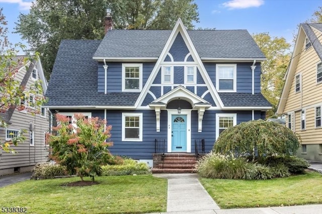 view of front of property with roof with shingles, a chimney, and a front lawn