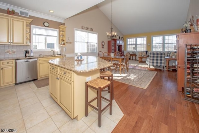 kitchen featuring dishwasher, a kitchen breakfast bar, light stone counters, cream cabinets, and a kitchen island