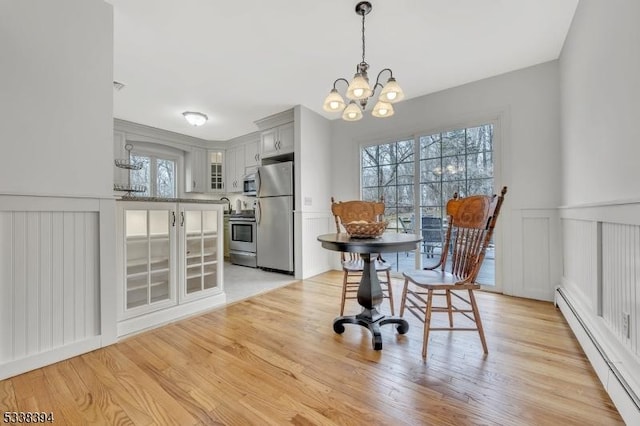 dining space with light wood-style floors, a baseboard heating unit, a chandelier, and wainscoting