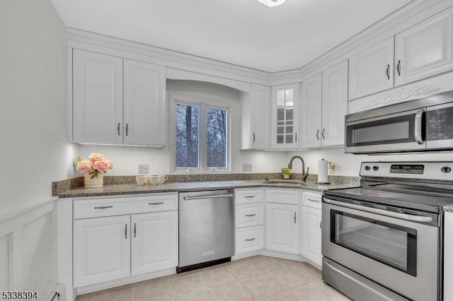 kitchen with white cabinets, a wainscoted wall, appliances with stainless steel finishes, dark stone countertops, and a sink