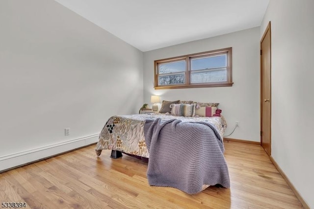 bedroom with light wood-type flooring, baseboards, and baseboard heating