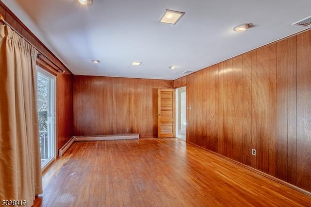 empty room with baseboard heating, wooden walls, and light hardwood / wood-style floors