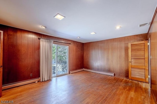 spare room with wooden walls, light hardwood / wood-style floors, and a baseboard heating unit