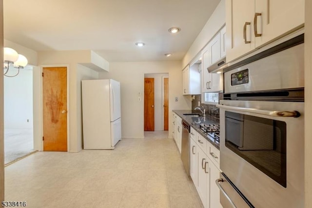 kitchen with appliances with stainless steel finishes, sink, dark stone counters, and white cabinets