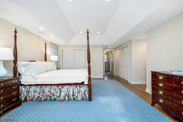 bedroom with a tray ceiling, hardwood / wood-style floors, and two closets