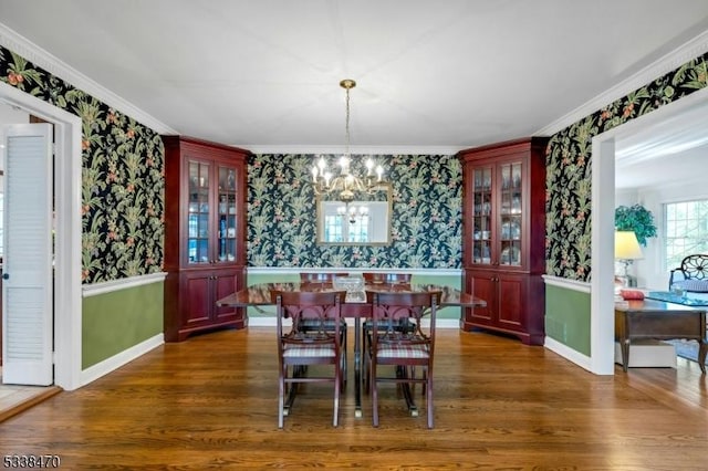 dining space featuring dark wood-type flooring, ornamental molding, and a notable chandelier