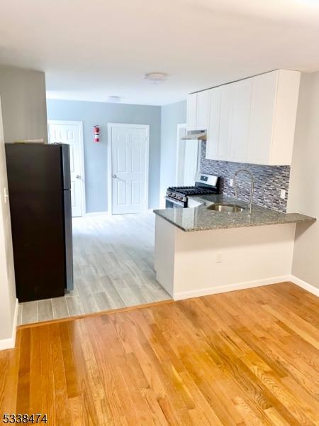 kitchen featuring white cabinetry, black fridge, stainless steel range with gas cooktop, kitchen peninsula, and dark stone counters