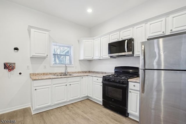 kitchen with appliances with stainless steel finishes, sink, white cabinetry, and light hardwood / wood-style floors