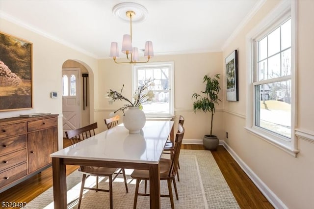 dining space with dark wood-type flooring, ornamental molding, and a notable chandelier