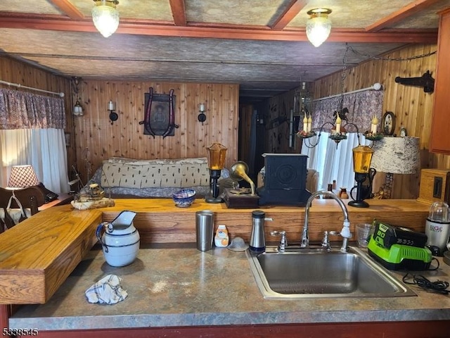 kitchen with beamed ceiling, sink, and wood walls