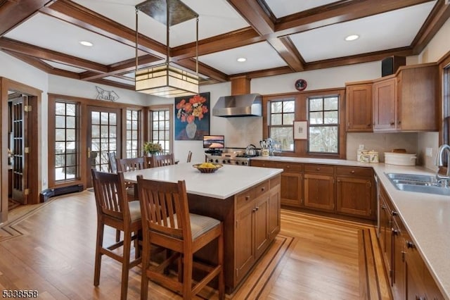 kitchen with a breakfast bar area, a sink, light countertops, wall chimney exhaust hood, and pendant lighting