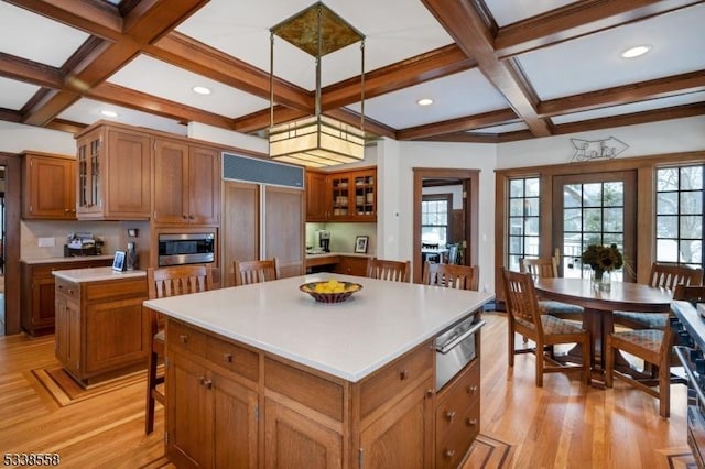 kitchen with pendant lighting, light countertops, glass insert cabinets, brown cabinetry, and a kitchen island