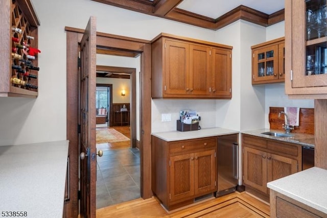 kitchen featuring refrigerator, a sink, light countertops, brown cabinetry, and glass insert cabinets