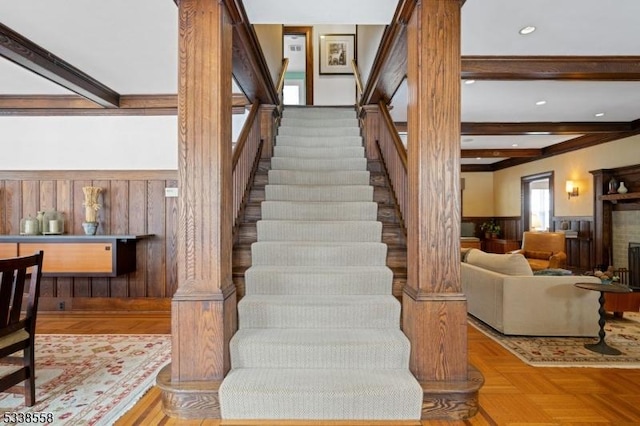 stairs with wood walls, a fireplace, beamed ceiling, and wainscoting