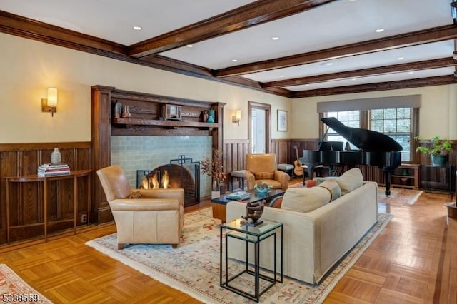 living room featuring a warm lit fireplace, beam ceiling, wainscoting, and crown molding