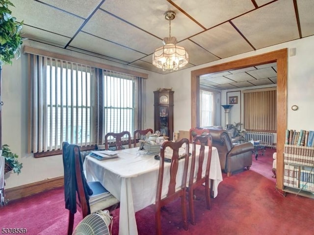 dining area with an inviting chandelier, a paneled ceiling, radiator heating unit, and carpet