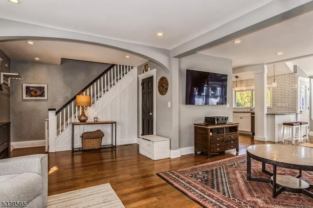 living area with arched walkways, recessed lighting, wood finished floors, baseboards, and stairs