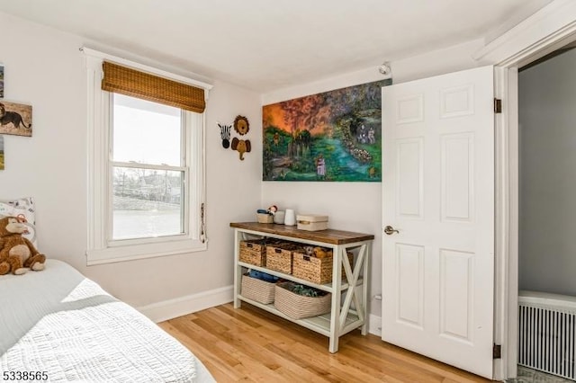 bedroom with radiator heating unit, baseboards, and light wood-style flooring