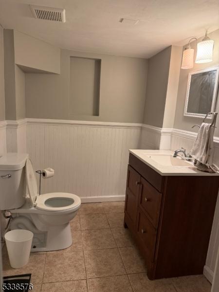 bathroom featuring a wainscoted wall, toilet, and visible vents