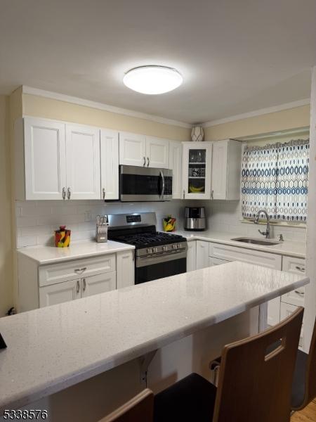 kitchen featuring a sink, stainless steel appliances, decorative backsplash, and white cabinetry