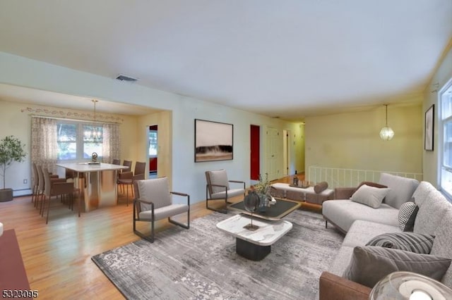 living room featuring an inviting chandelier, light wood-type flooring, and baseboard heating