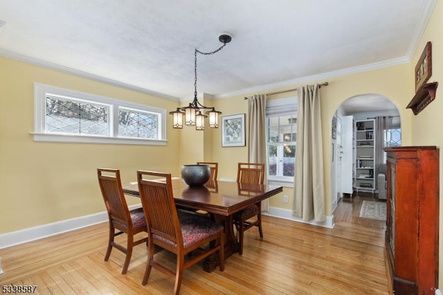 dining room featuring light wood-style flooring, arched walkways, baseboards, and ornamental molding