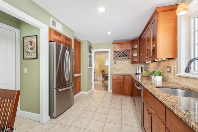 kitchen featuring a sink, visible vents, appliances with stainless steel finishes, light stone countertops, and glass insert cabinets