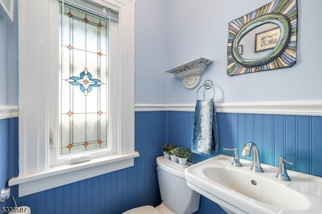 half bathroom featuring a wainscoted wall, a sink, and toilet