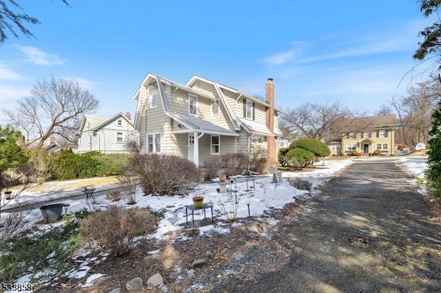 view of snowy exterior featuring a residential view, a chimney, and a gambrel roof