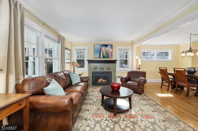 living area featuring a wealth of natural light, crown molding, light wood-style flooring, and a tiled fireplace