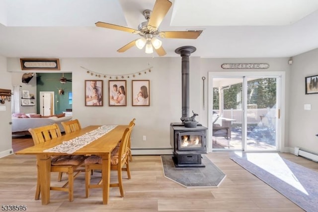 dining area with a baseboard heating unit, a wood stove, light wood-type flooring, and ceiling fan