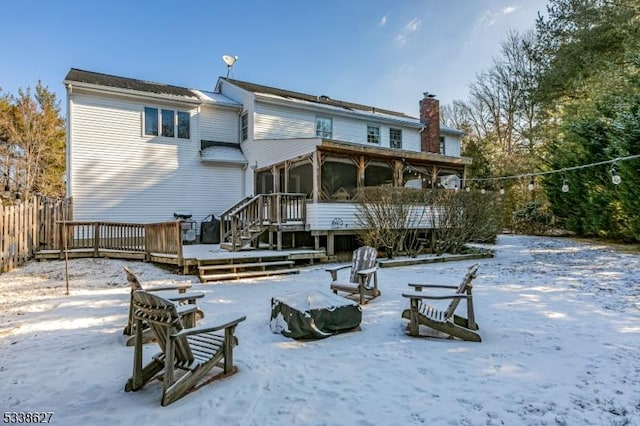 snow covered rear of property with a deck and a sunroom