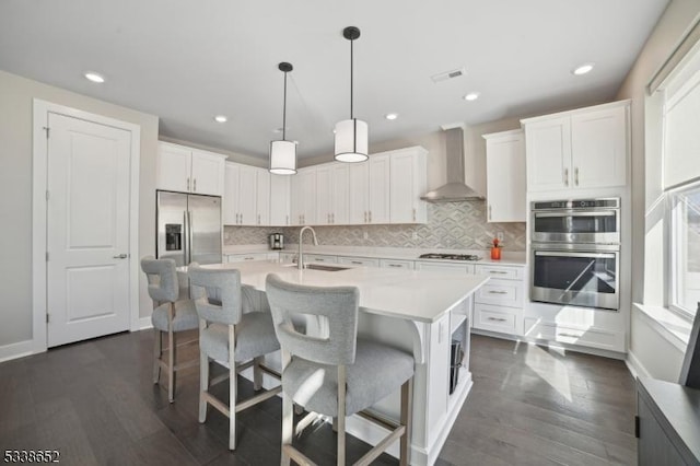 kitchen with light countertops, appliances with stainless steel finishes, white cabinets, a sink, and wall chimney exhaust hood