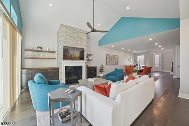 living area featuring high vaulted ceiling, a stone fireplace, a ceiling fan, baseboards, and dark wood-style floors