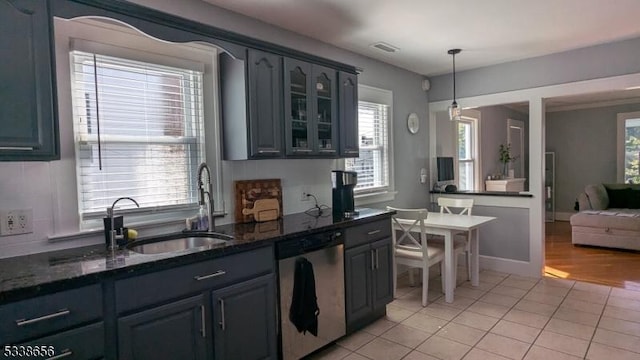 kitchen with light tile patterned floors, dark stone countertops, glass insert cabinets, and stainless steel dishwasher