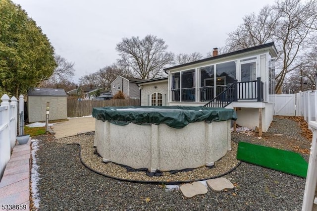 rear view of property featuring a sunroom, a covered pool, and a storage unit