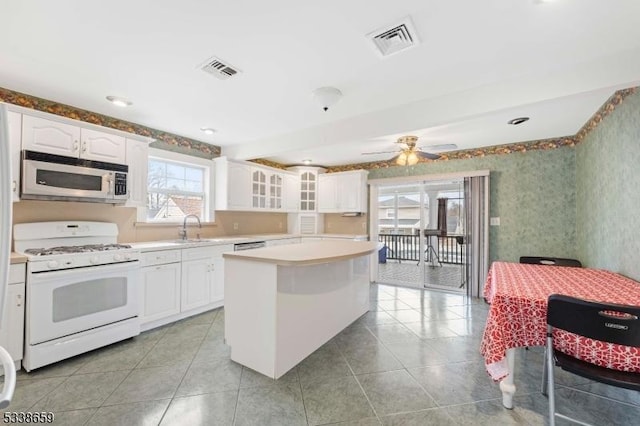 kitchen featuring sink, light tile patterned floors, white range with gas stovetop, white cabinetry, and a center island