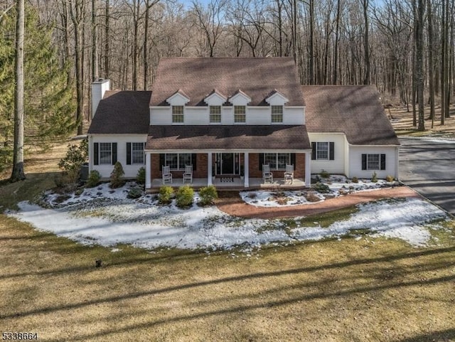 cape cod house with driveway, a front lawn, a chimney, and a porch