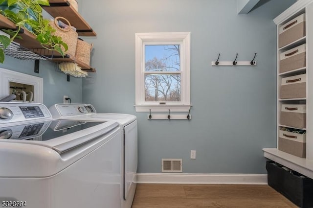 laundry area featuring washing machine and clothes dryer, visible vents, wood finished floors, laundry area, and baseboards