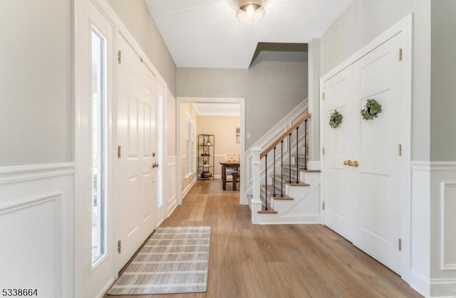 foyer with stairs, a wainscoted wall, light wood-style flooring, and a decorative wall